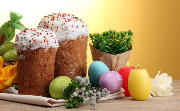 Beaux gâteaux de Pâques, oeufs colorés et bougies sur table en bois sur fond jaune — Photo
