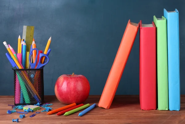 Kokoonpano kirjoja, paperitavarat ja omena opettajan pöydälle taustalla liitutaulu — kuvapankkivalokuva