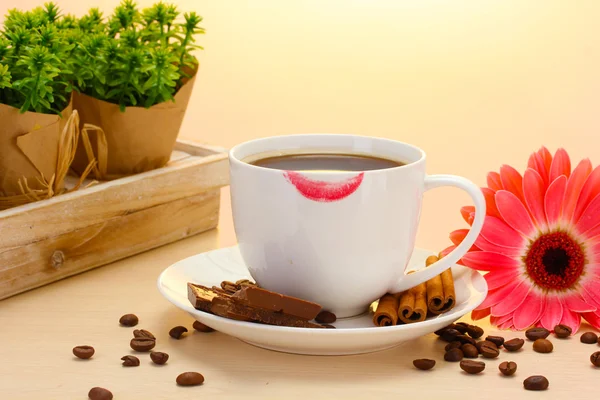 Šálek kávy s rtěnkou mark a gerbera fazole, skořice hole na dřevěný stůl — Stock fotografie