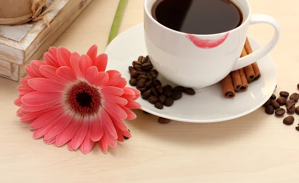 Taza de café con marca de lápiz labial y granos de gerberas, palitos de canela en la mesa de madera —  Fotos de Stock