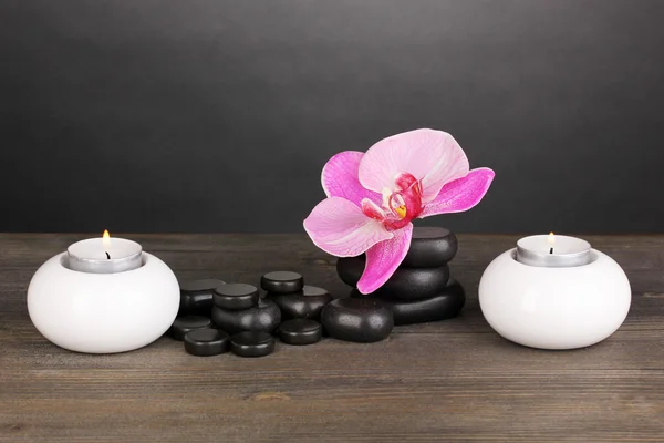 Σπα πέτρες με ορχιδέα λουλούδι και κεριά στο ξύλινο τραπέζι σε γκρι φόντο — Φωτογραφία Αρχείου