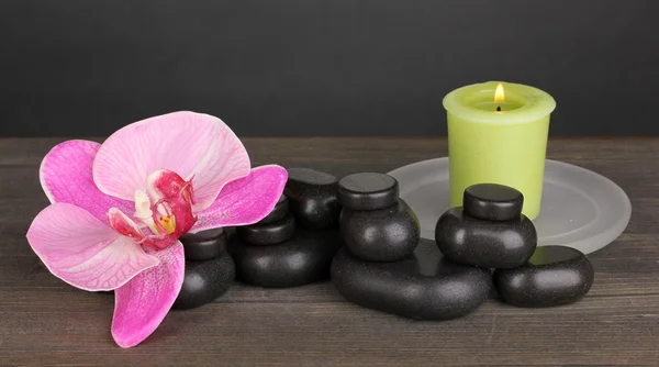 Pedras de spa com flor de orquídea e vela na mesa de madeira no fundo cinza — Fotografia de Stock