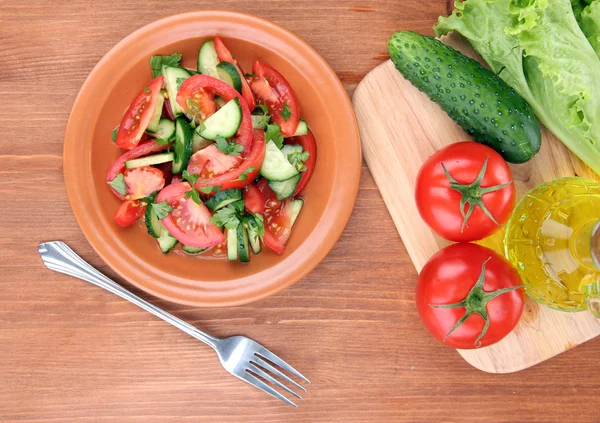 Čerstvý salát s rajčaty a okurkami na dřevěné pozadí — Stock fotografie