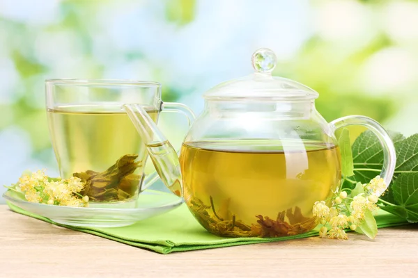 Teáskanna és a csésze linden tea és a virágok, a kertben fából készült asztal — Stock Fotó