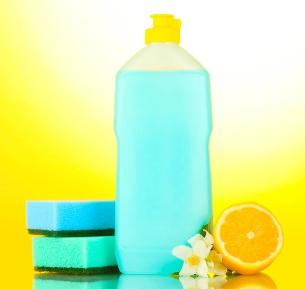 Folyékony mosogatószer, szivacsok és a citrom, a virágok sárga háttér — Stock Fotó