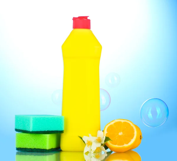 Spülmittel mit Schwämmen und Zitrone mit Blumen auf blauem Hintergrund — Stockfoto