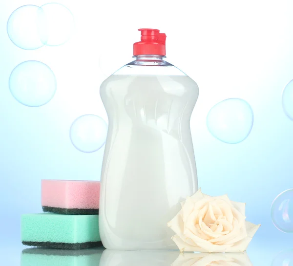 Líquido de lavagem de pratos com esponjas e flores sobre fundo azul — Fotografia de Stock