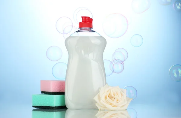 Liquido per lavastoviglie con spugne e fiori su sfondo blu — Foto Stock