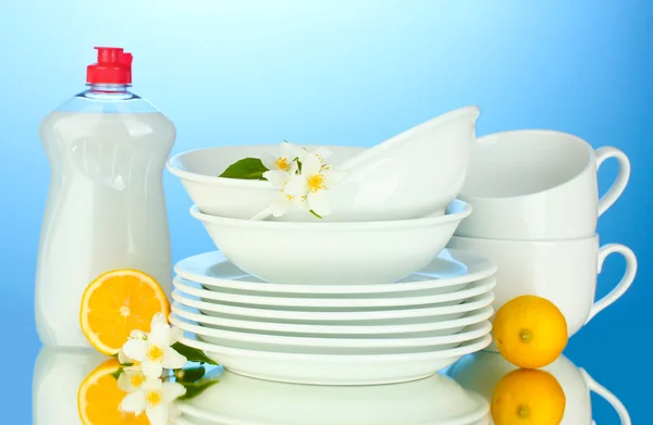 Platos y tazas limpias vacías con líquido lavavajillas y limón sobre fondo azul —  Fotos de Stock