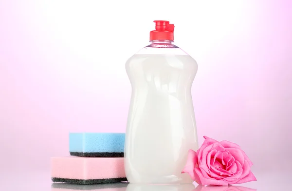 Líquido lavavajillas con esponjas y flores sobre fondo rosa — Foto de Stock