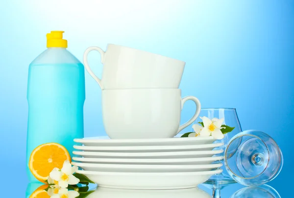 Άδειο καθαρά πιάτα, ποτήρια και κύπελλα με υγρό πιάτων και λεμόνι σε μπλε φόντο — Φωτογραφία Αρχείου