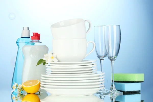 Lege schoon borden, glazen en cups met afwasmiddel, sponzen en citroen op blauwe achtergrond — Stockfoto