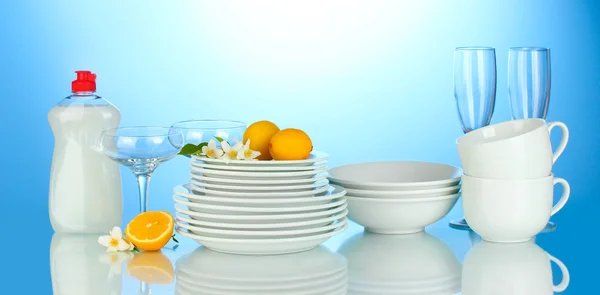 Pratos limpos vazios, copos e copos com liquido de lavagem de louça e limão no fundo azul — Fotografia de Stock