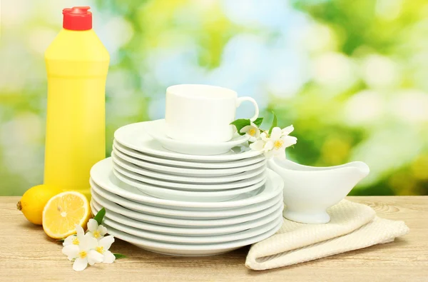 Boş temiz tabak ve bardaklar bulaşık deterjanı, çiçek ve limonlu yeşil zemin üzerine ahşap tablo — Stok fotoğraf