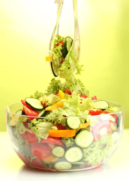 Insalata di verdure fresche in ciotola trasparente con cucchiaio e forchetta su fondo verde — Foto Stock