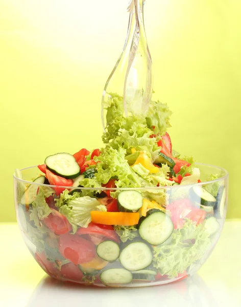 Ensalada de verduras frescas en un tazón transparente con cuchara y tenedor sobre fondo verde — Foto de Stock