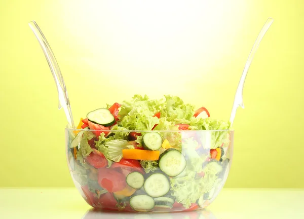 Sałatką ze świeżych warzyw w przejrzysty miski z łyżka i widelec na zielonym tle — Zdjęcie stockowe