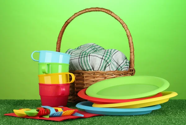 stock image Bright plastic disposable tableware and picnic basket on the lawn on colorful background