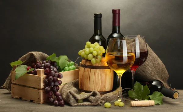 Barrel, bottles and glasses of wine and ripe grapes on wooden table on grey background — Stock Photo, Image