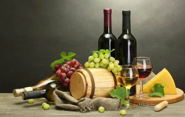 Fat, flaskor och glas vin, ost och mogna druvor på träbord på grå bakgrund — Stockfoto