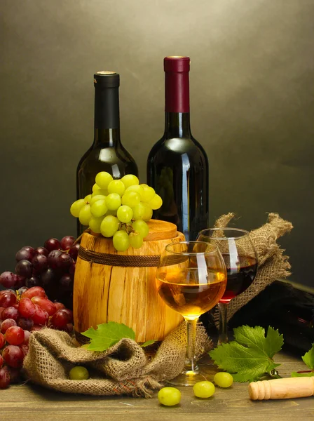 Бочка, бутылки и бокалы вина и спелый виноград на деревянном столе на сером фоне — стоковое фото