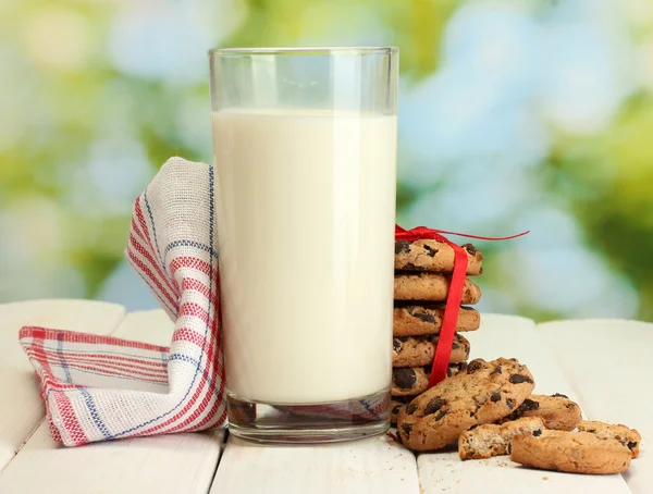Ποτήρι γάλα, σοκολάτα τσιπ cookies με κόκκινη κορδέλα και αγριολούλουδα στον ξύλινο τραπέζι σε πράσινο φόντο — Φωτογραφία Αρχείου