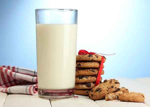 Szklankę mleka i czekolady chipy ciasteczka z czerwoną wstążką na drewnianym stole na niebieskim tle — Zdjęcie stockowe
