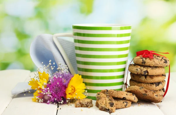 Kopje melk, chocolade chips cookies met rood lint en wilde bloemen op houten tafel op groene achtergrond — Stockfoto