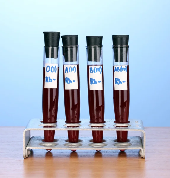 Tubos de ensaio com sangue sobre mesa de madeira sobre fundo azul — Fotografia de Stock