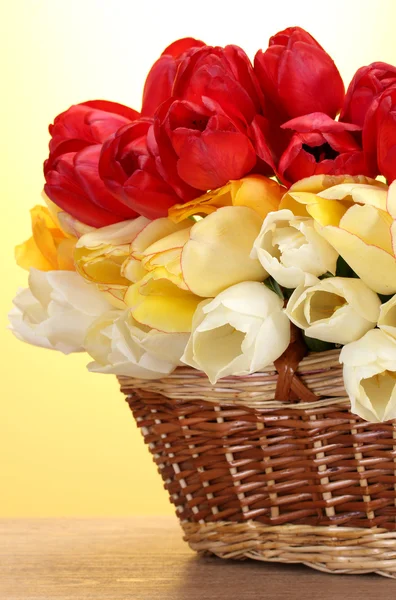 Bellissimi tulipani in cesto su tavolo di legno su sfondo giallo — Foto Stock