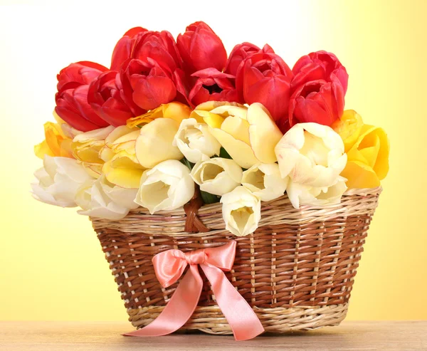 Beautiful tulips in basket on wooden table on yellow background — Stock Photo, Image