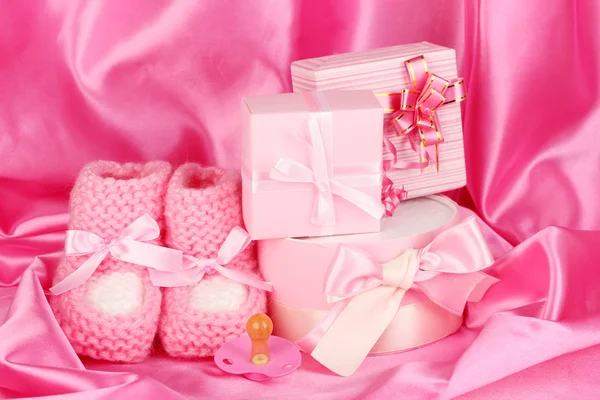 Botas de bebé rosa, chupete, regalos sobre fondo de seda — Foto de Stock