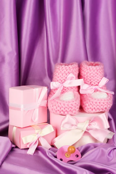 Pink baby boots, pacifier, gifts on silk background — Stock Photo, Image
