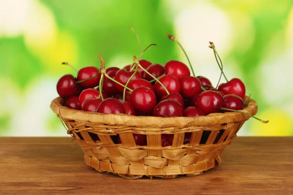 Cherry in wicker bowl on wooden table on green background — Stock Photo, Image