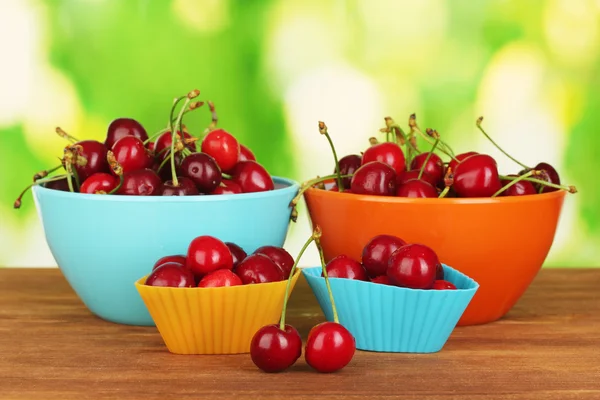Bowls and cutters with cherries on wooden table on green background — Stock Photo, Image