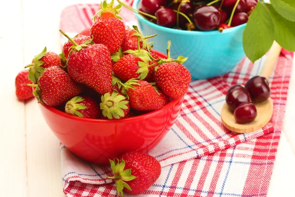 Ripe strawberries and cherry berries in bowls on white wooden table — Stock Photo, Image