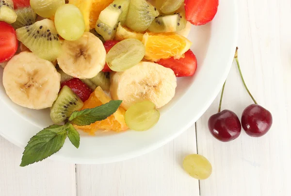 Salada de frutas frescas em prato e bagas em mesa de madeira branca — Fotografia de Stock