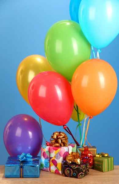 Balões coloridos segurando um presentes em uma mesa de madeira no fundo azul — Fotografia de Stock