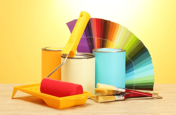 Boya, rulo, fırça ve parlak renk sarı zemin üzerine ahşap masa üzerinde paleti teneke kutular — Stok fotoğraf