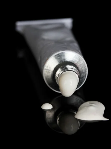 White paint follows from the tube on black background close-up — Stock Photo, Image