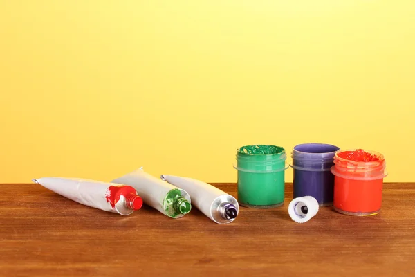 Tubi con acquerelli colorati e vasetti con guazzo su tavolo in legno su sfondo luminoso — Foto Stock