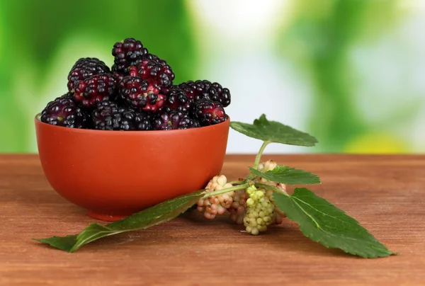 Ceramical bowl with ripe mulberries on wooden table on bright green background close-up — Stock Photo, Image