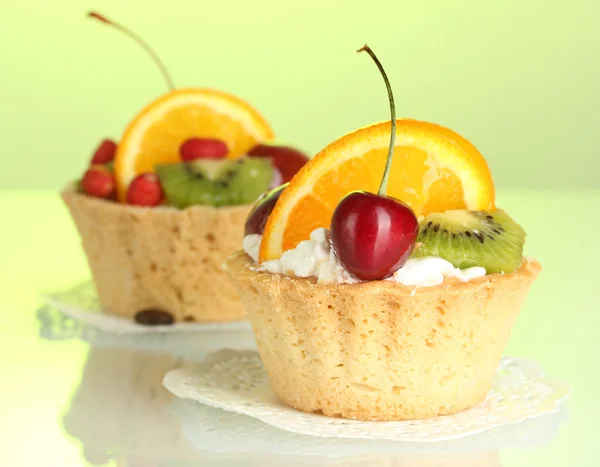 Sweet cakes with fruits on green background — Stock Photo, Image