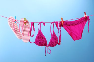 Women's swimsuit and flip-flops hanging on a rope on blue background clipart