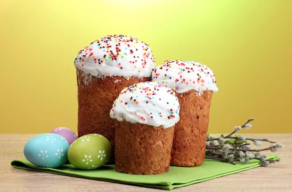 Beautiful Easter cakes, colorful eggs and pussy-willow twigs on wooden table on yellow background — Stock Photo, Image