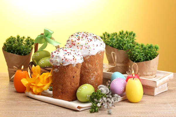 Belos bolos de Páscoa, ovos coloridos e velas na mesa de madeira no fundo amarelo — Fotografia de Stock