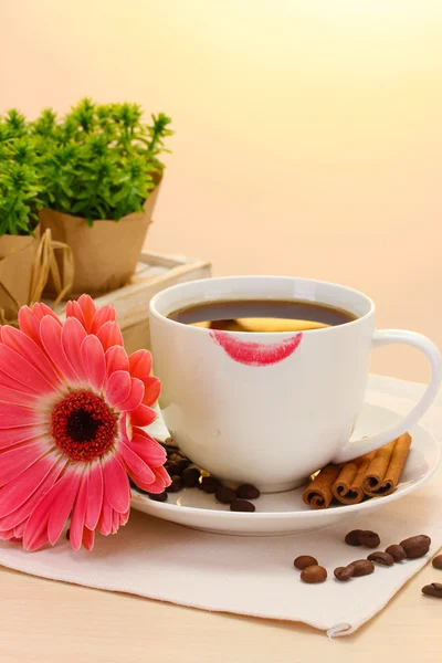 Kopp kaffe med läppstift mark och gerbera bönor, kanel pinnar på träbord — Stockfoto