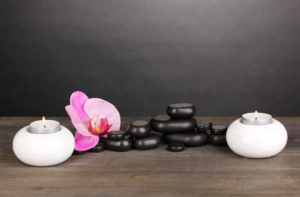 Pedras de spa com flor de orquídea e velas na mesa de madeira no fundo cinza — Fotografia de Stock