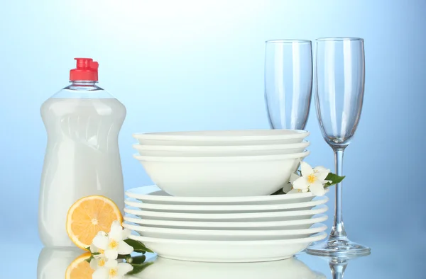 Empty clean plates and glasses with dishwashing liquid and lemon on blue background — Stock Photo, Image