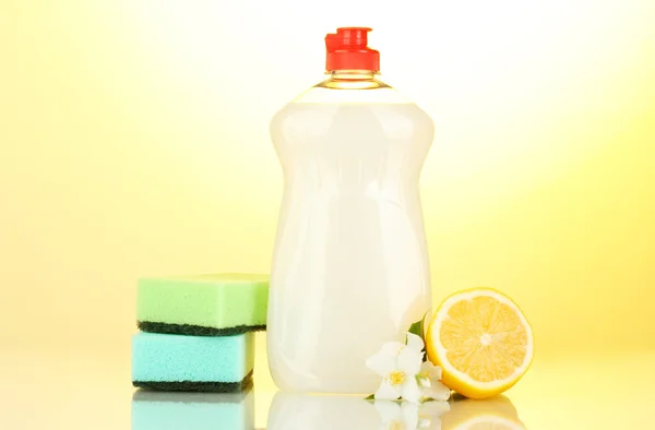 Dishwashing liquid with sponges and lemon with flowers on yellow background — Stock Photo, Image